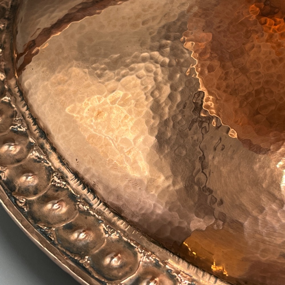A hand-hammered copper tazza featuring twin side handles, a circular pedestal base, and a stamped geometric border along the shallow bowl rim. View XX