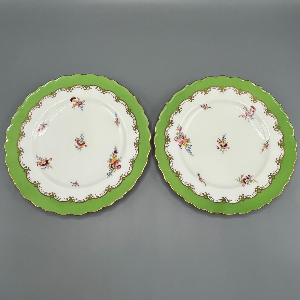 A pair of Victorian Coalport porcelain plates with bright green scalloped borders, gilded scrollwork, and hand-painted floral sprays on white centres.