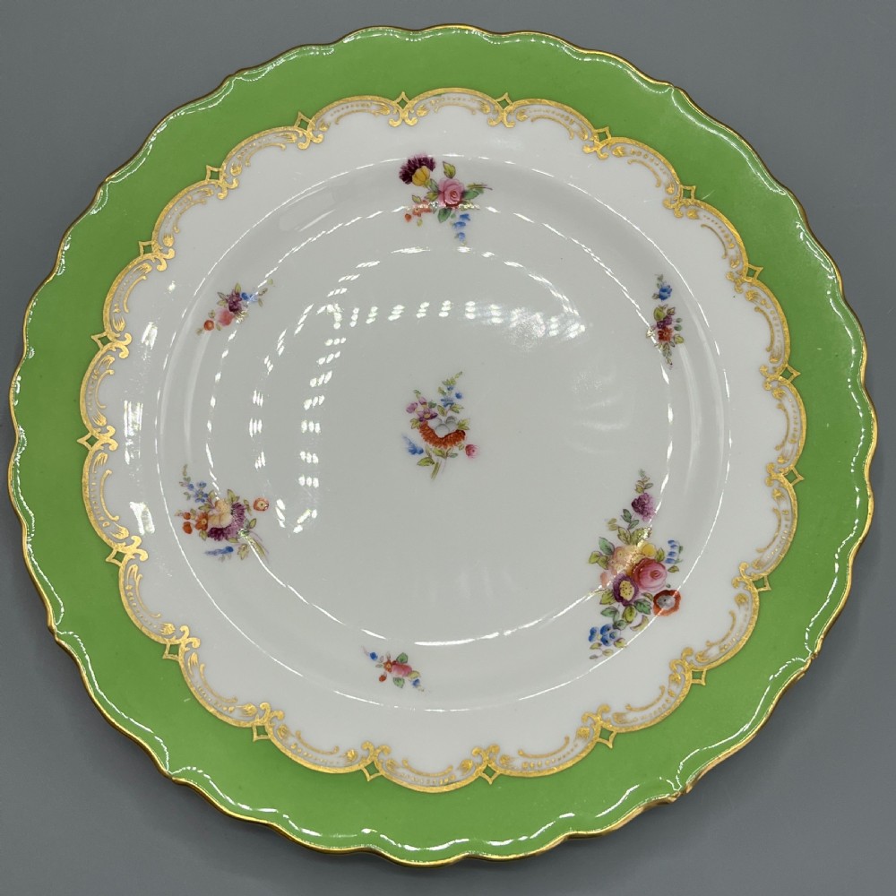 A pair of Victorian Coalport porcelain plates with bright green scalloped borders, gilded scrollwork, and hand-painted floral sprays on white centres. View X
