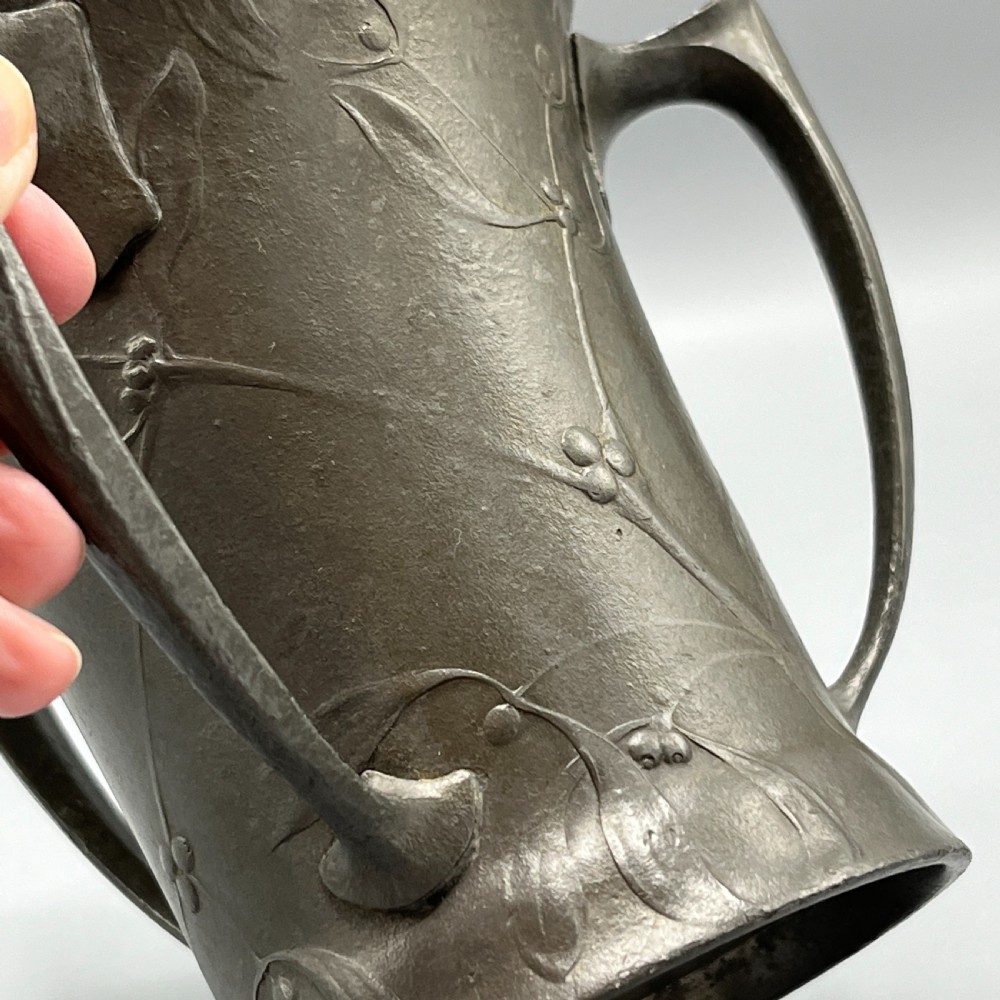 A grey pewter Art Nouveau tyg vase featuring three curved handles and relief-moulded mistletoe motifs around the body. View VII