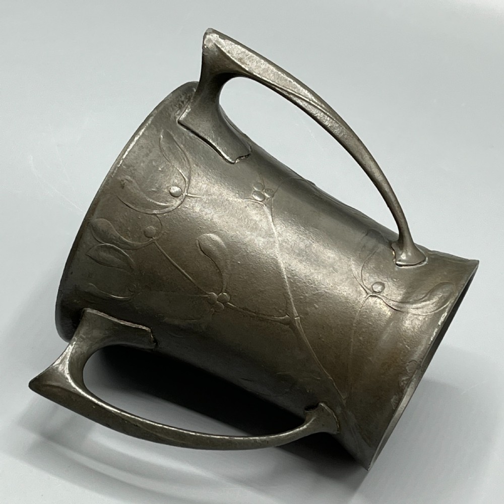 A grey pewter Art Nouveau tyg vase featuring three curved handles and relief-moulded mistletoe motifs around the body. View VIII