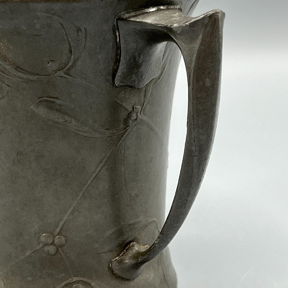 A grey pewter Art Nouveau tyg vase featuring three curved handles and relief-moulded mistletoe motifs around the body. View IX