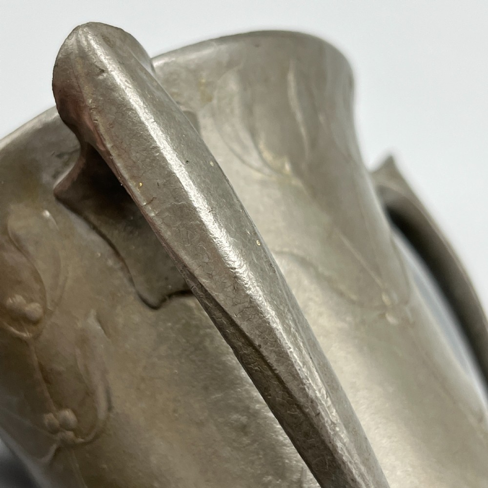 A grey pewter Art Nouveau tyg vase featuring three curved handles and relief-moulded mistletoe motifs around the body. View XIII
