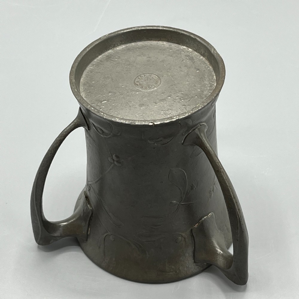 A grey pewter Art Nouveau tyg vase featuring three curved handles and relief-moulded mistletoe motifs around the body. View XVI