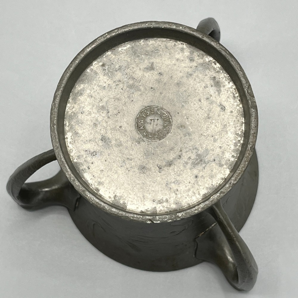 A grey pewter Art Nouveau tyg vase featuring three curved handles and relief-moulded mistletoe motifs around the body. View XVIII