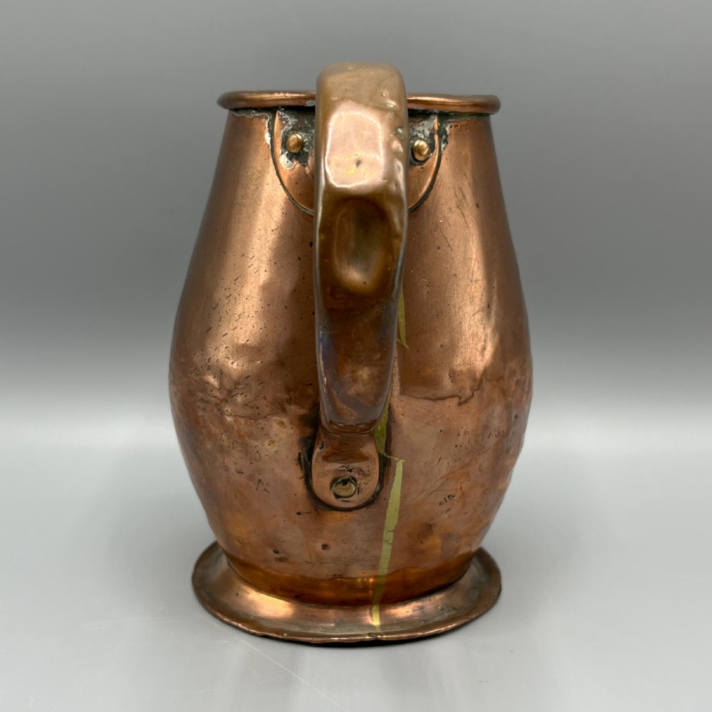An antique Georgian copper jug featuring a hand-hammered body, wide pouring spout, flared base, and a riveted loop handle. View II