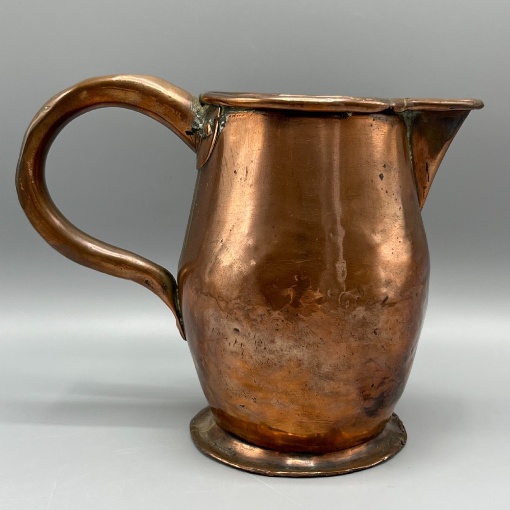 An antique Georgian copper jug featuring a hand-hammered body, wide pouring spout, flared base, and a riveted loop handle. View IV