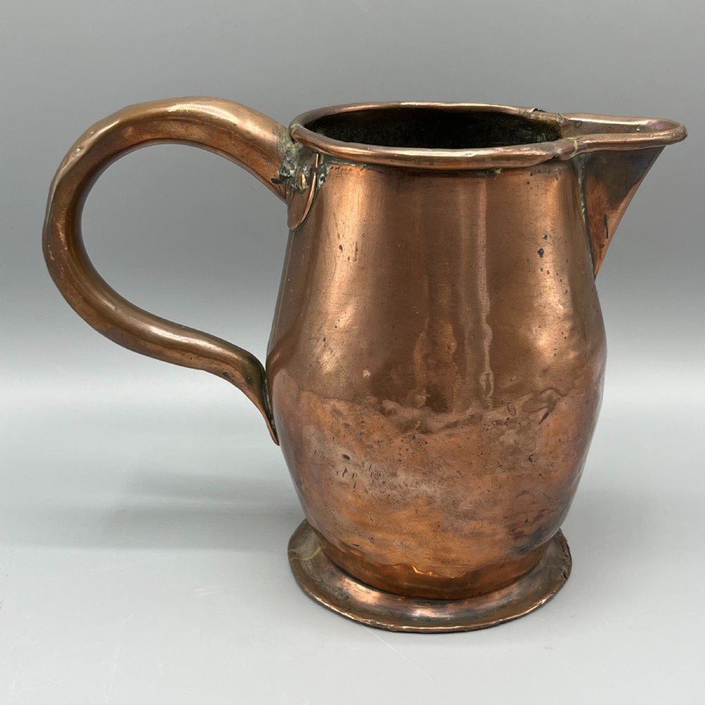 An antique Georgian copper jug featuring a hand-hammered body, wide pouring spout, flared base, and a riveted loop handle. View V