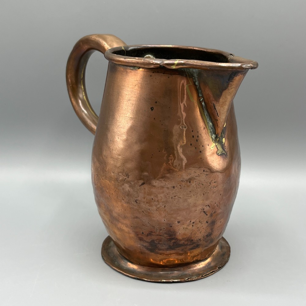 An antique Georgian copper jug featuring a hand-hammered body, wide pouring spout, flared base, and a riveted loop handle. View VI