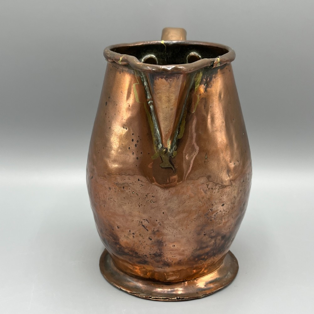 An antique Georgian copper jug featuring a hand-hammered body, wide pouring spout, flared base, and a riveted loop handle. View VII