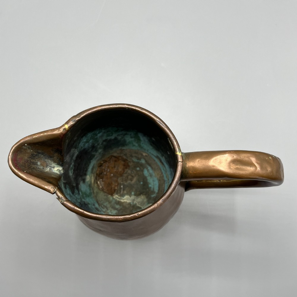 An antique Georgian copper jug featuring a hand-hammered body, wide pouring spout, flared base, and a riveted loop handle. View X