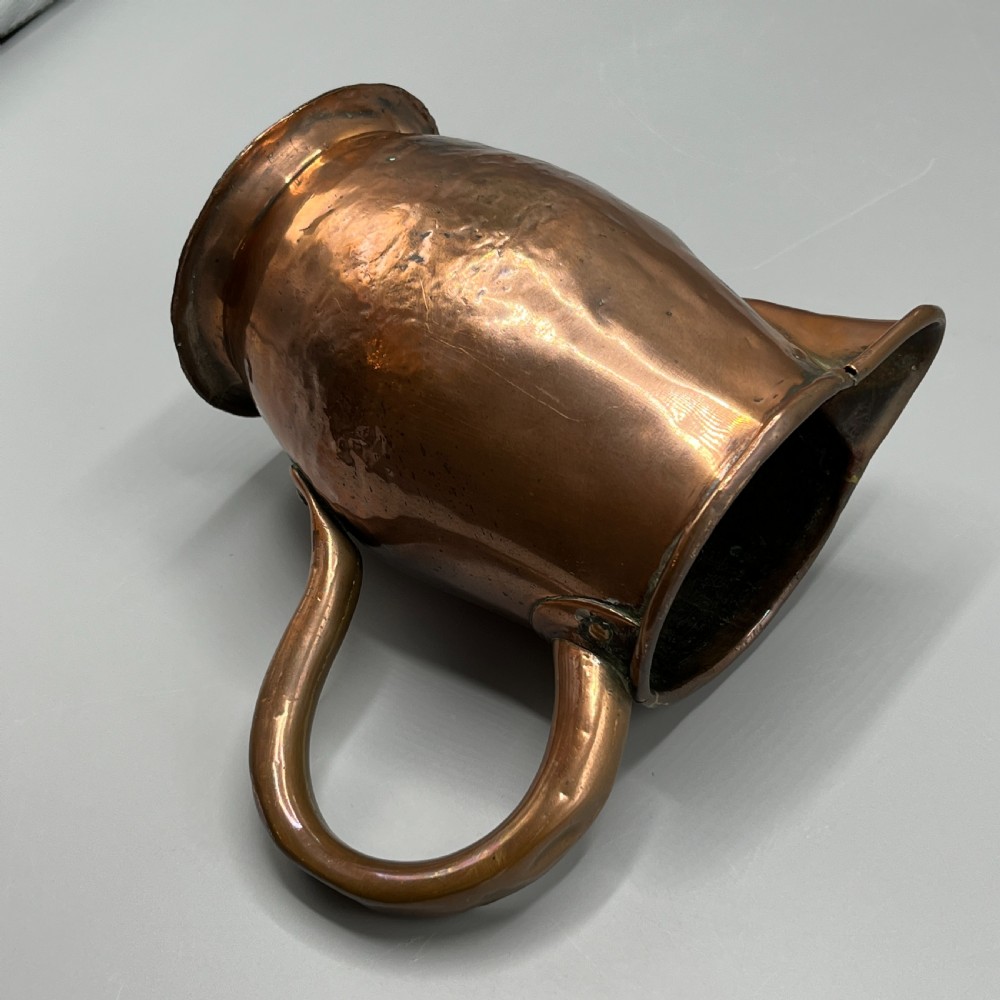 An antique Georgian copper jug featuring a hand-hammered body, wide pouring spout, flared base, and a riveted loop handle. View XI