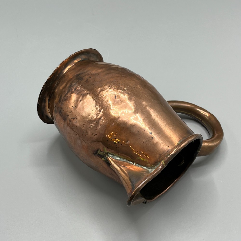An antique Georgian copper jug featuring a hand-hammered body, wide pouring spout, flared base, and a riveted loop handle. View XII