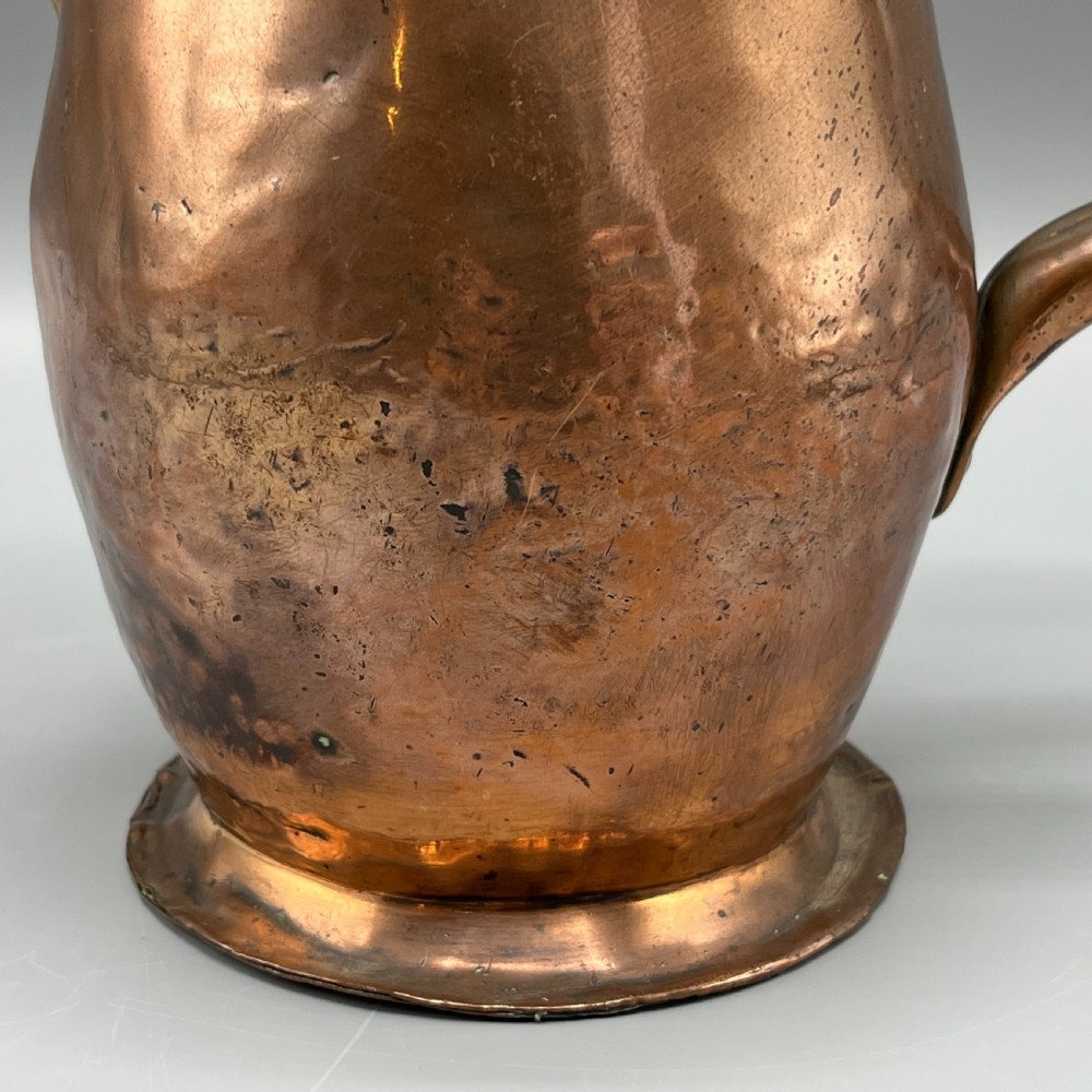An antique Georgian copper jug featuring a hand-hammered body, wide pouring spout, flared base, and a riveted loop handle. View XIII