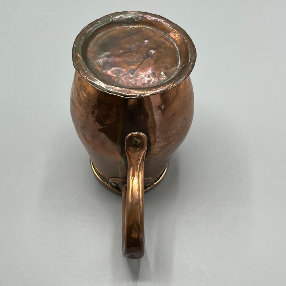 An antique Georgian copper jug featuring a hand-hammered body, wide pouring spout, flared base, and a riveted loop handle. View XVII