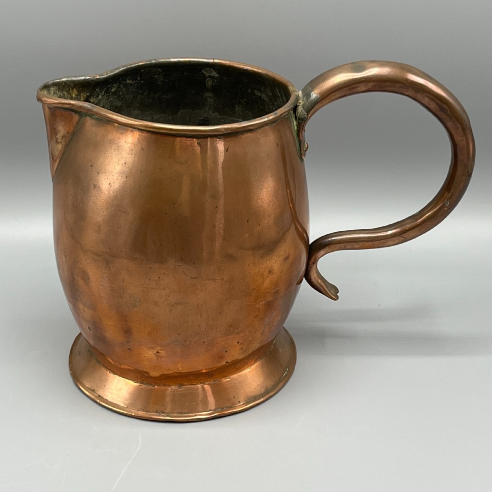 A Georgian copper jug featuring a bulbous body, a flared circular base, a pinched pouring spout, and a large curved loop handle.
