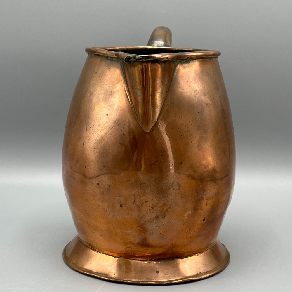 A Georgian copper jug featuring a bulbous body, a flared circular base, a pinched pouring spout, and a large curved loop handle. View X