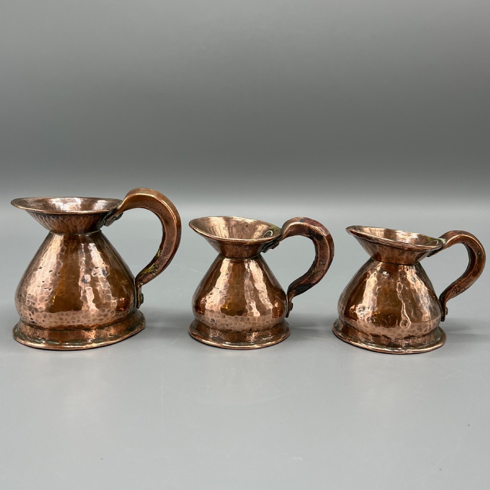 A set of three graduated Victorian copper miniature jugs with hand-hammered surfaces and flared spouts.