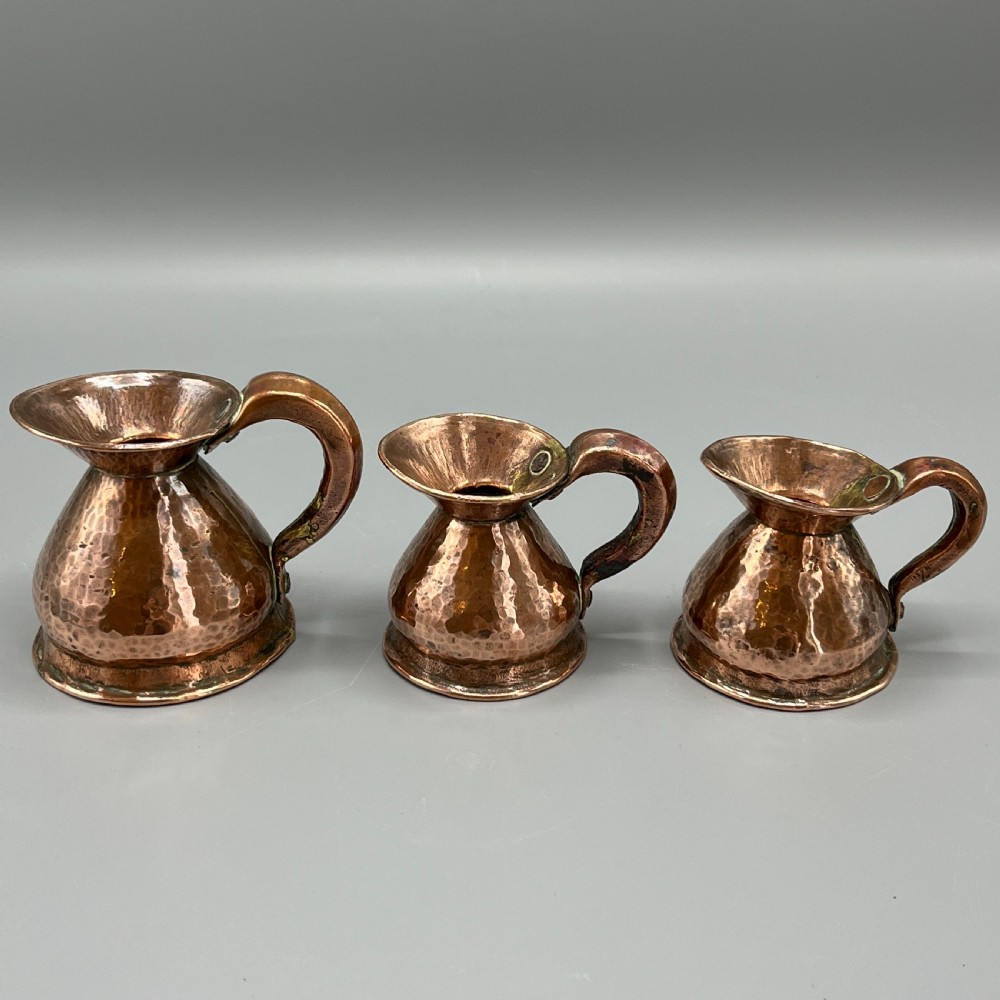A set of three graduated Victorian copper miniature jugs with hand-hammered surfaces and flared spouts. View II