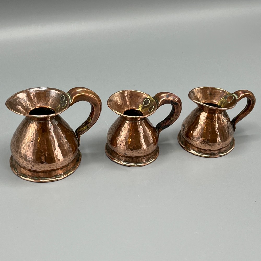 A set of three graduated Victorian copper miniature jugs with hand-hammered surfaces and flared spouts. View III