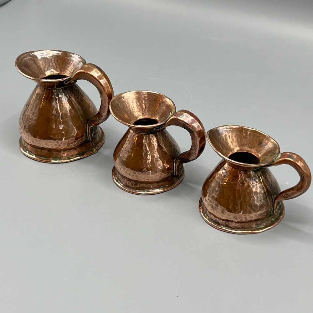 A set of three graduated Victorian copper miniature jugs with hand-hammered surfaces and flared spouts. View IV