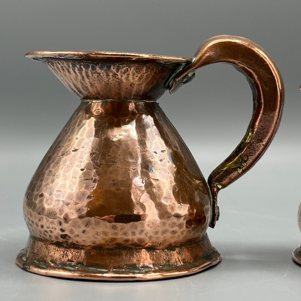 A set of three graduated Victorian copper miniature jugs with hand-hammered surfaces and flared spouts. View V