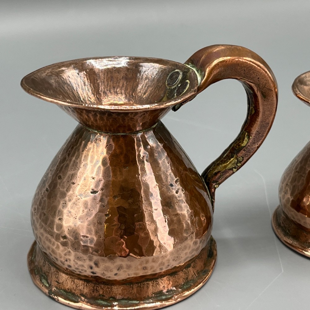 A set of three graduated Victorian copper miniature jugs with hand-hammered surfaces and flared spouts. View VI