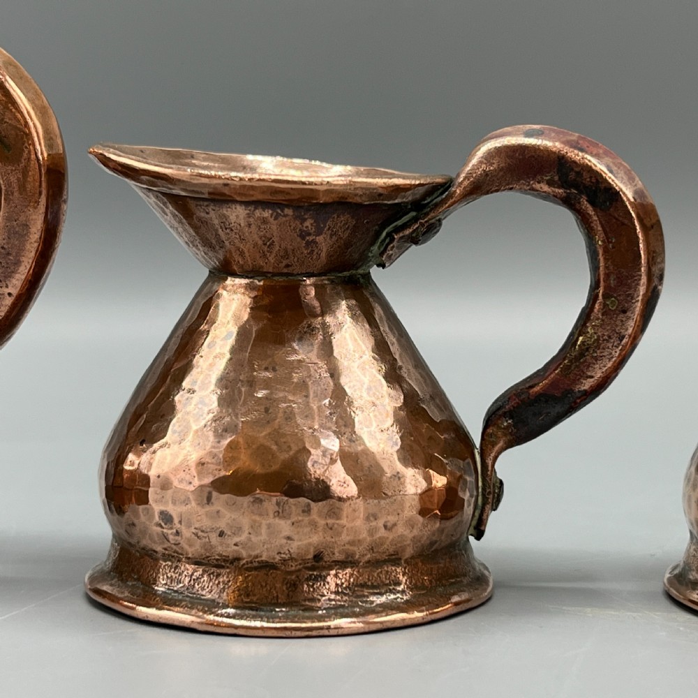 A set of three graduated Victorian copper miniature jugs with hand-hammered surfaces and flared spouts. View VII