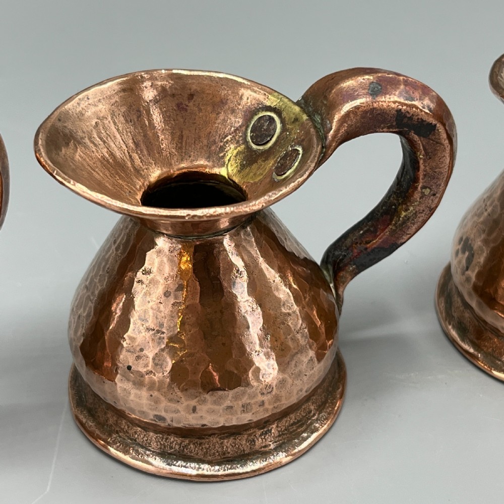 A set of three graduated Victorian copper miniature jugs with hand-hammered surfaces and flared spouts. View VIII