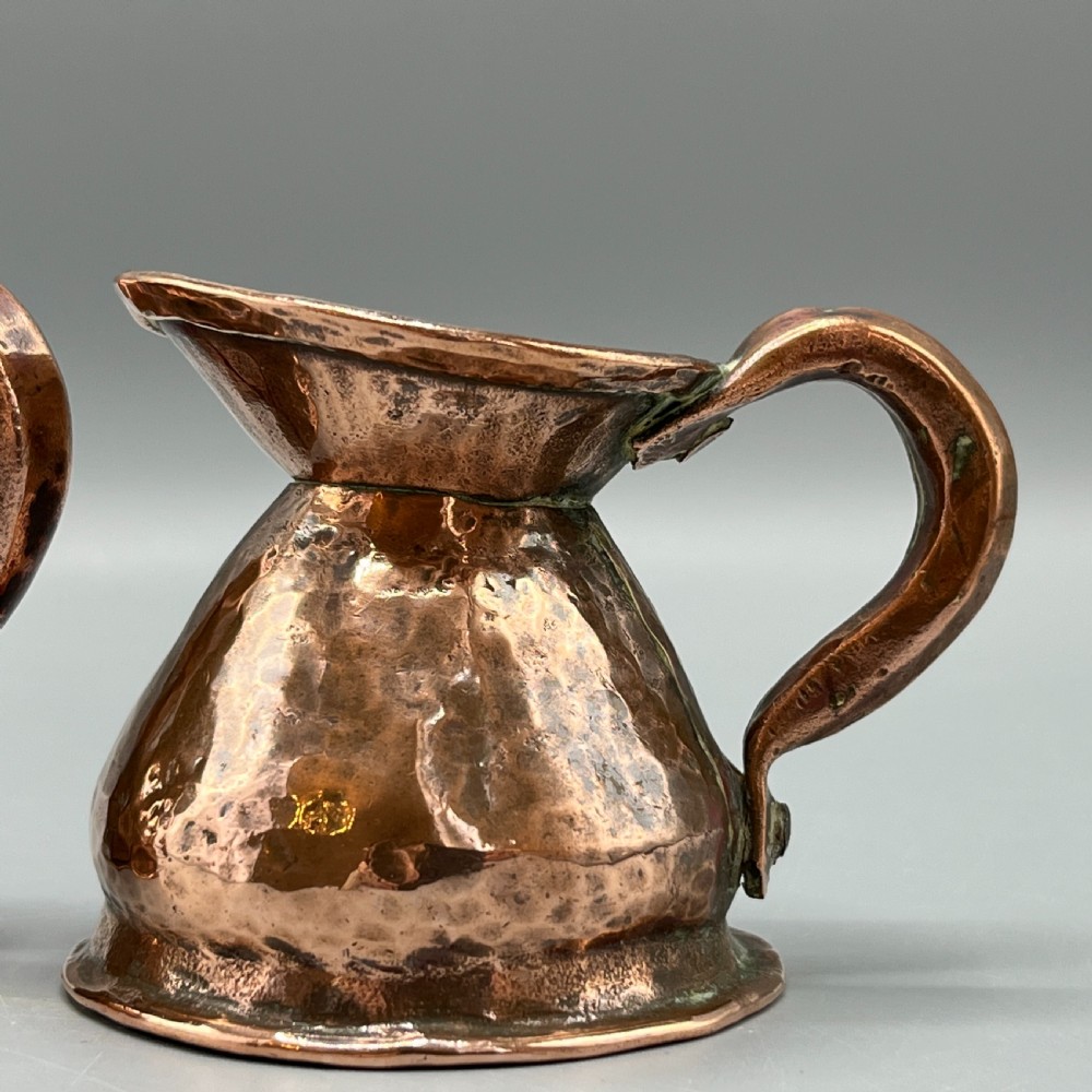 A set of three graduated Victorian copper miniature jugs with hand-hammered surfaces and flared spouts. View IX