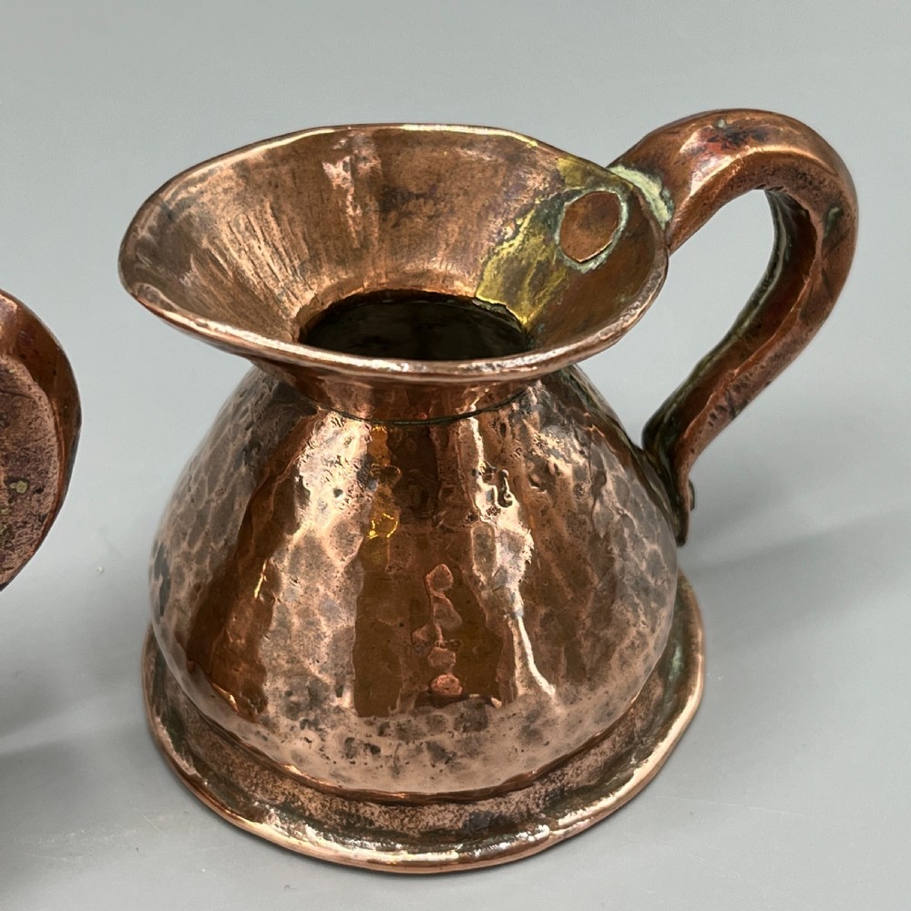 A set of three graduated Victorian copper miniature jugs with hand-hammered surfaces and flared spouts. View X