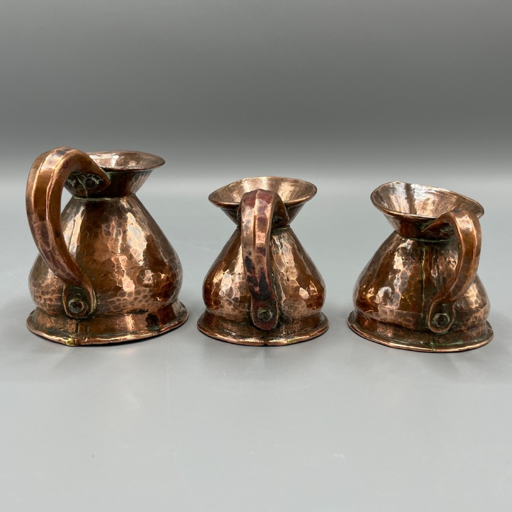 A set of three graduated Victorian copper miniature jugs with hand-hammered surfaces and flared spouts. View XI