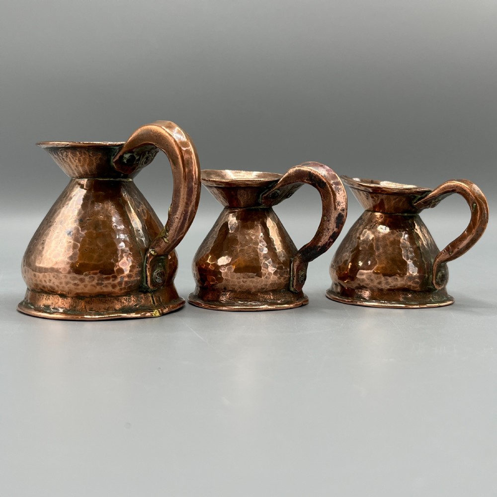 A set of three graduated Victorian copper miniature jugs with hand-hammered surfaces and flared spouts. View XII