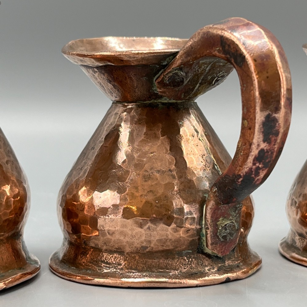 A set of three graduated Victorian copper miniature jugs with hand-hammered surfaces and flared spouts. View XIV