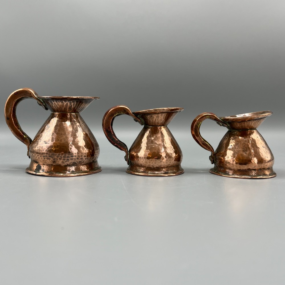A set of three graduated Victorian copper miniature jugs with hand-hammered surfaces and flared spouts. View XVI
