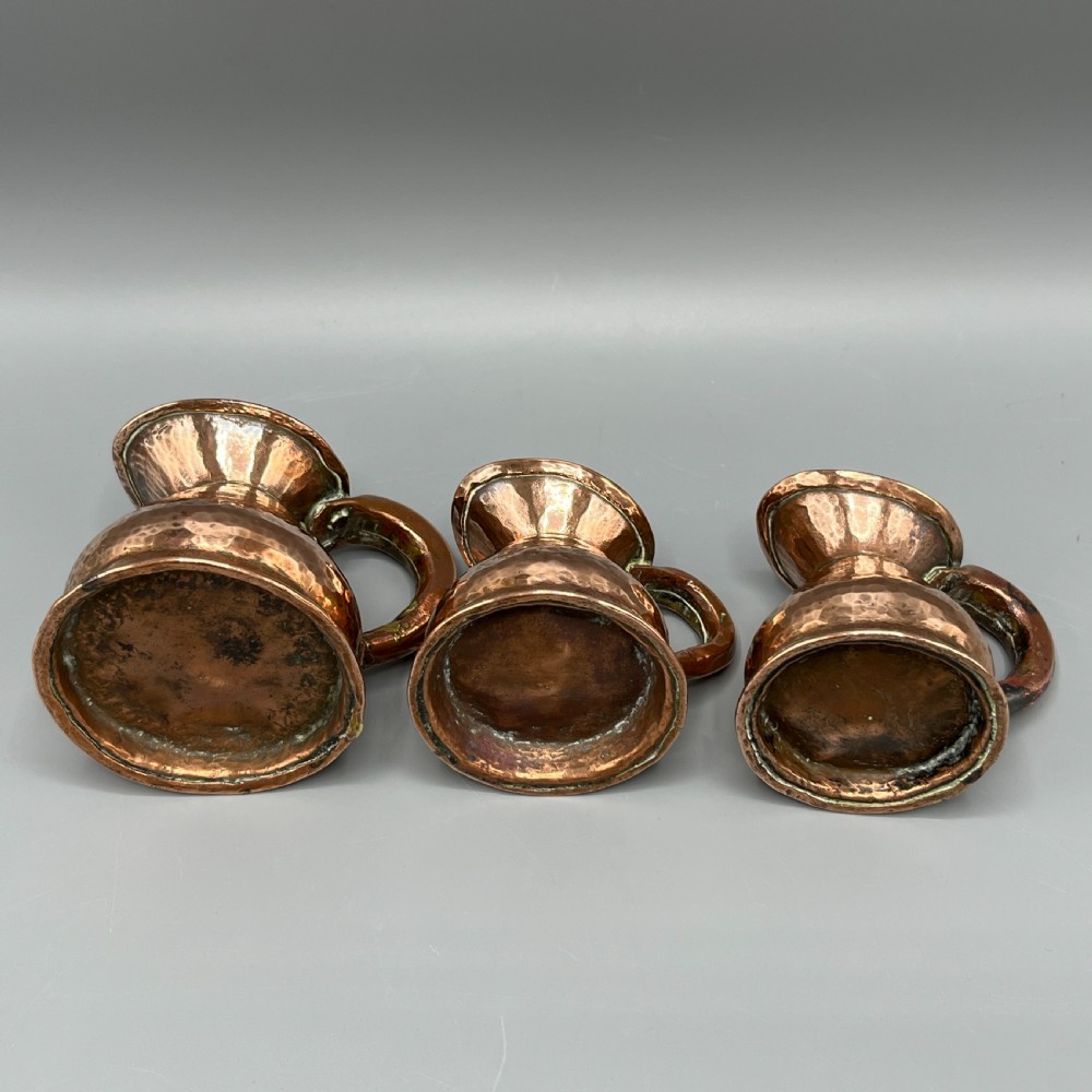 A set of three graduated Victorian copper miniature jugs with hand-hammered surfaces and flared spouts. View XVIII