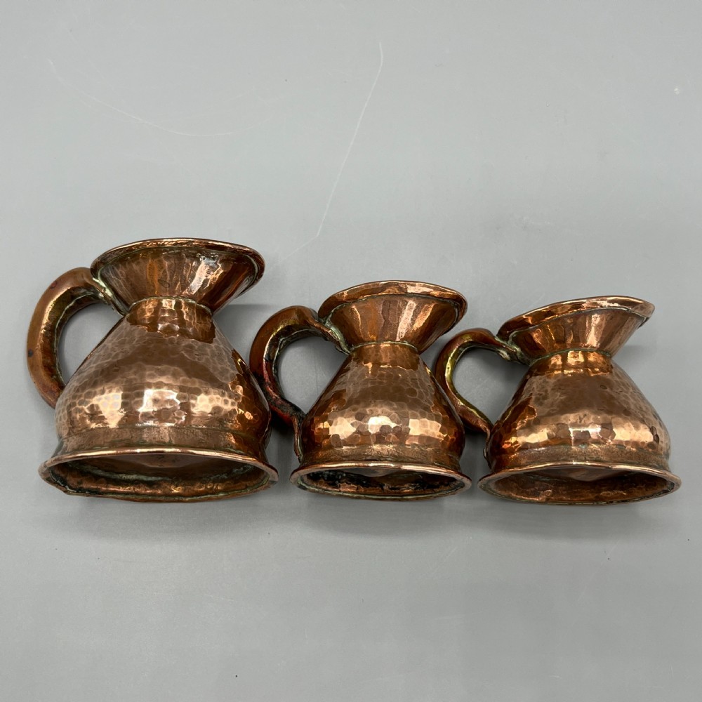 A set of three graduated Victorian copper miniature jugs with hand-hammered surfaces and flared spouts. View XXI