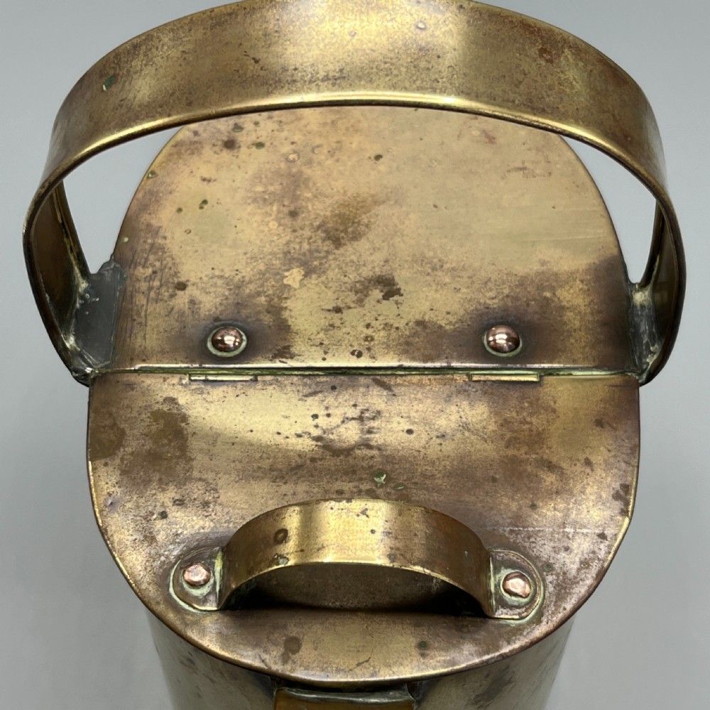 An Edwardian brass hot water or watering can featuring an oval body, fixed overhead flat strap handle, rear loop, diagonal spout, and visible copper rivets. View VIII