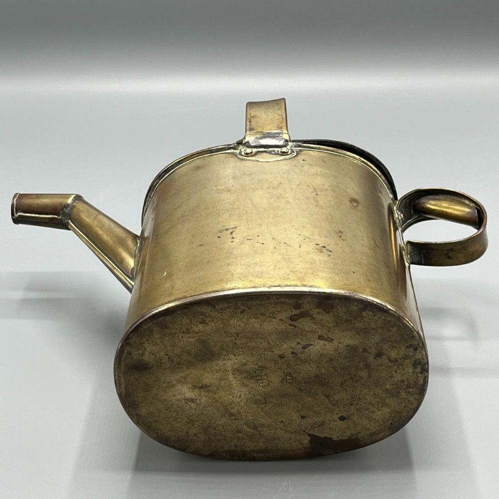An Edwardian brass hot water or watering can featuring an oval body, fixed overhead flat strap handle, rear loop, diagonal spout, and visible copper rivets. View XII