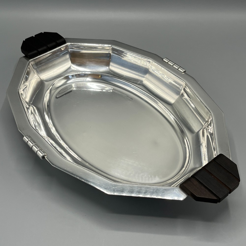 An octagonal silver-plated serving dish featuring faceted sides and carved dark wooden handles on opposite ends.