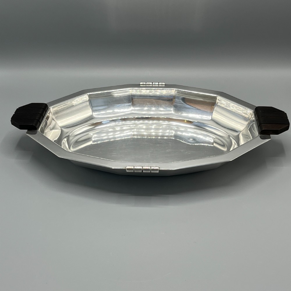 An octagonal silver-plated serving dish featuring faceted sides and carved dark wooden handles on opposite ends. View VI