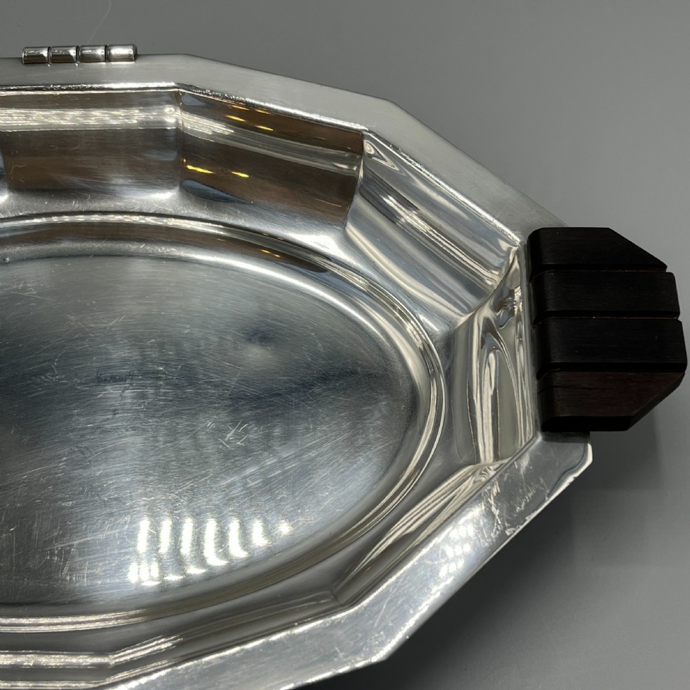 An octagonal silver-plated serving dish featuring faceted sides and carved dark wooden handles on opposite ends. View XV