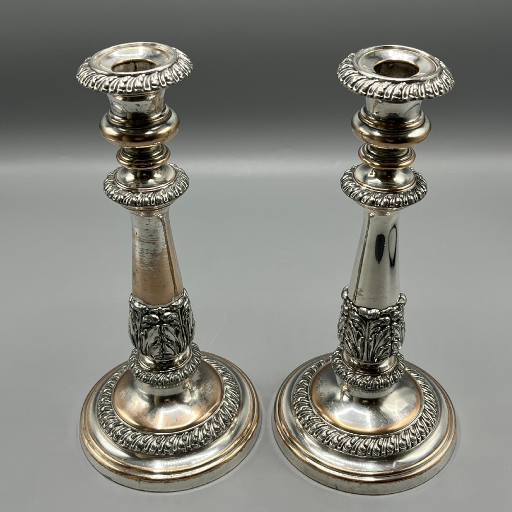 A pair of antique silver-plated candlesticks with gadrooned rims, acanthus leaf details, and exposed copper highlights on round bases.