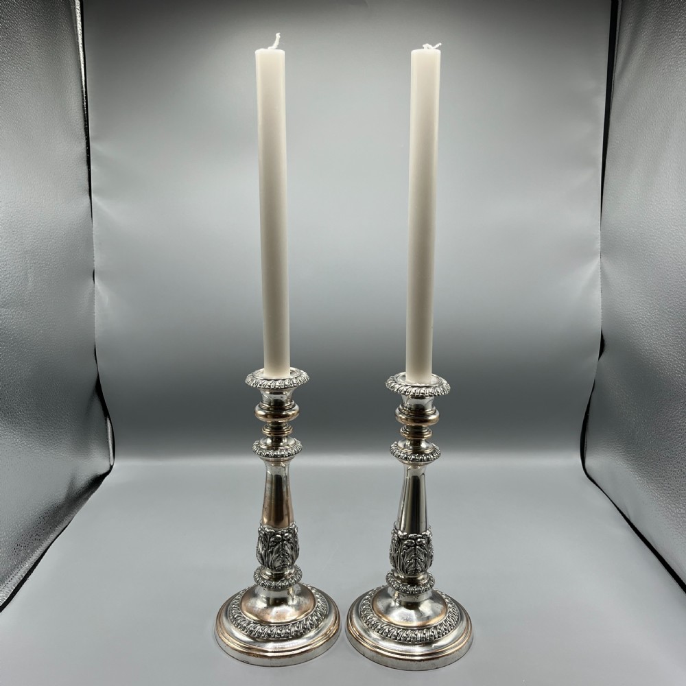 A pair of antique silver-plated candlesticks with gadrooned rims, acanthus leaf details, and exposed copper highlights on round bases. View IV