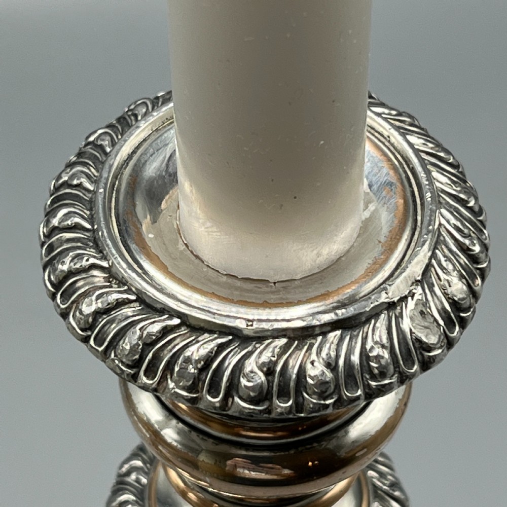 A pair of antique silver-plated candlesticks with gadrooned rims, acanthus leaf details, and exposed copper highlights on round bases. View V