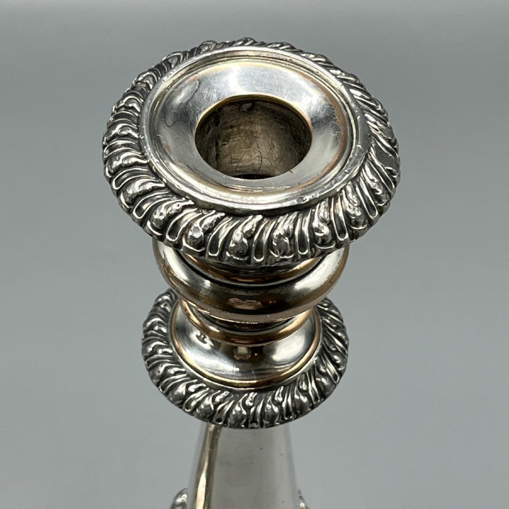 A pair of antique silver-plated candlesticks with gadrooned rims, acanthus leaf details, and exposed copper highlights on round bases. View VI