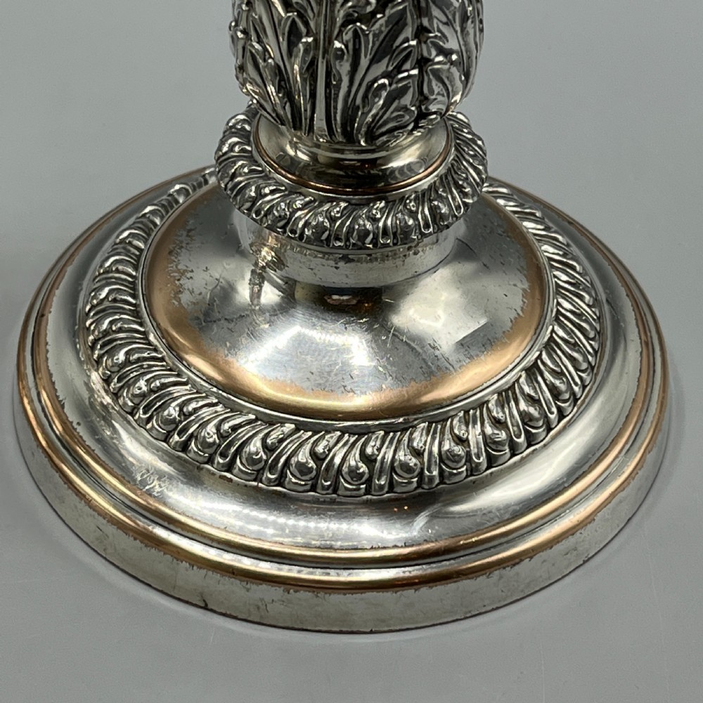 A pair of antique silver-plated candlesticks with gadrooned rims, acanthus leaf details, and exposed copper highlights on round bases. View VII