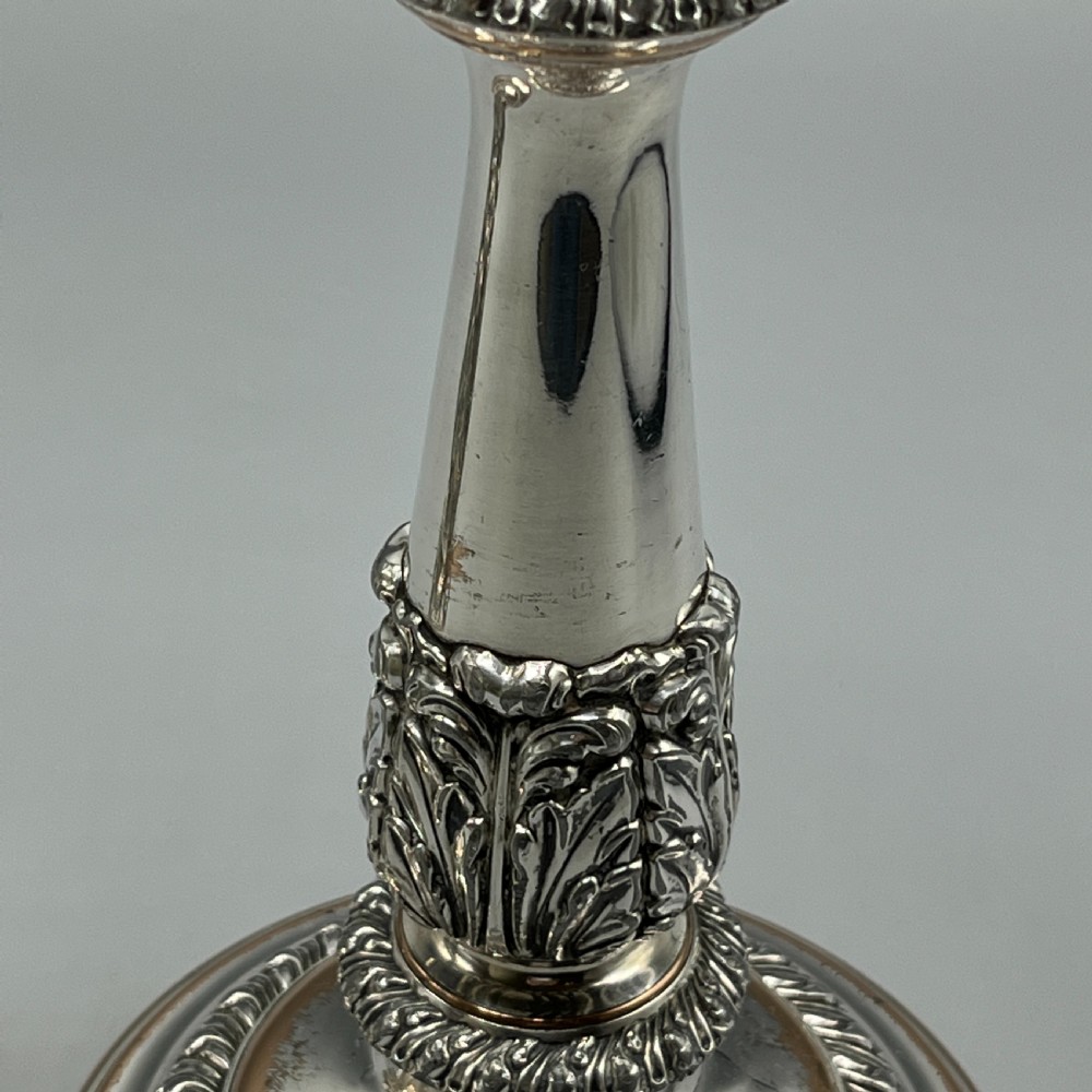 A pair of antique silver-plated candlesticks with gadrooned rims, acanthus leaf details, and exposed copper highlights on round bases. View VIII