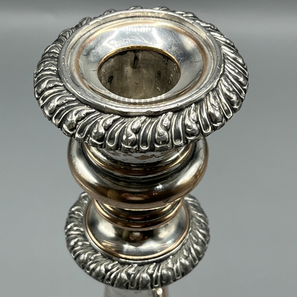 A pair of antique silver-plated candlesticks with gadrooned rims, acanthus leaf details, and exposed copper highlights on round bases. View IX