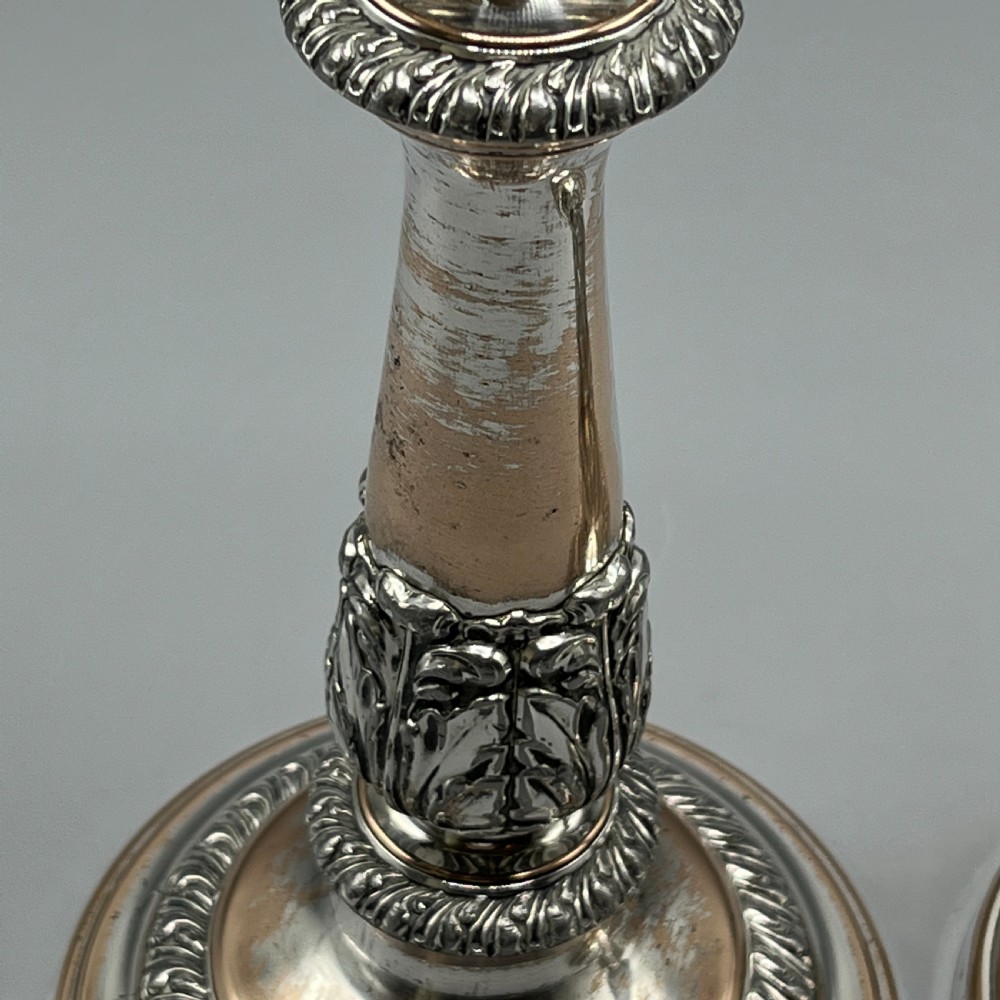 A pair of antique silver-plated candlesticks with gadrooned rims, acanthus leaf details, and exposed copper highlights on round bases. View X